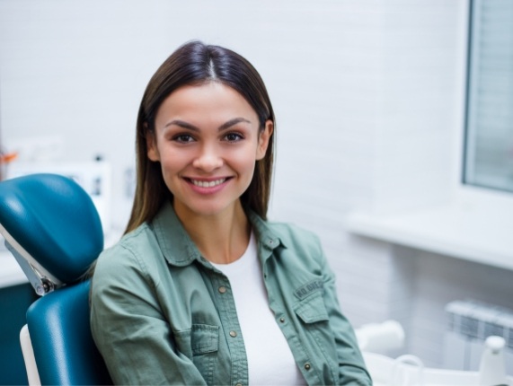 Young woman in dark green jacket smiling while sitting in dental chair