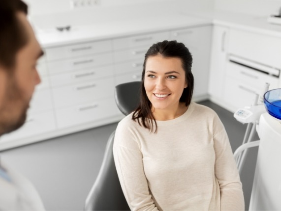 Young woman in white sweater smiling while talking to her dentist