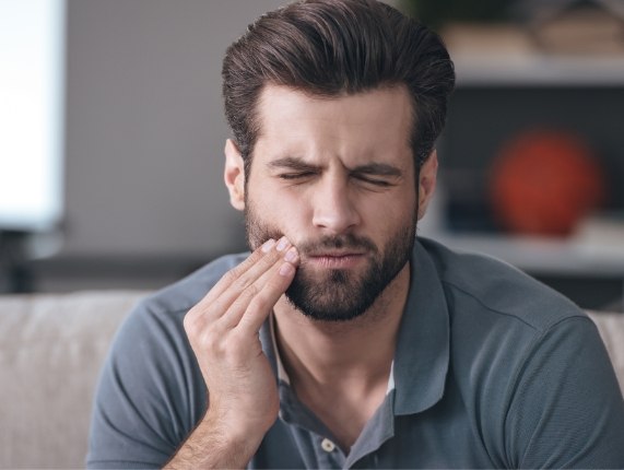 Man in gray polo shirt holding his cheek in pain