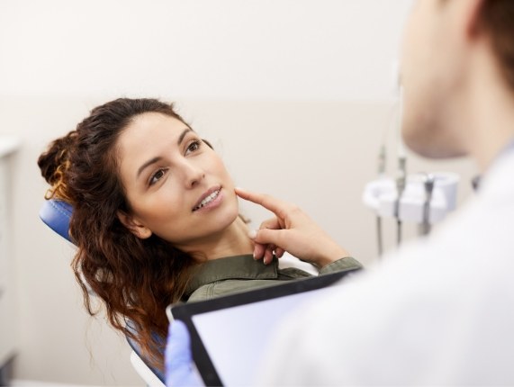 Woman pointing to her cheek while talking to her dentist