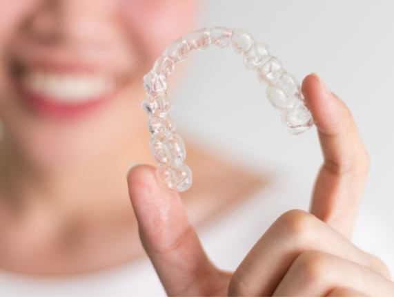 Smiling person holding Invisalign clear aligner