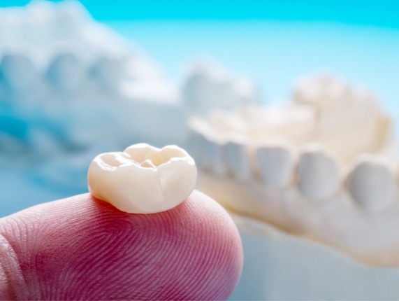 Close up of person holding a dental crown on their finger