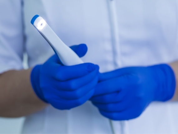 Two gloved hands holding a thin white intraoral camera