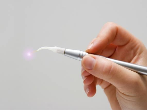 Hand holding a thin silver dental soft tissue laser