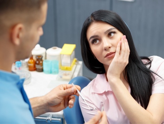 Woman holding her cheek in pain while talking to emergency dentist