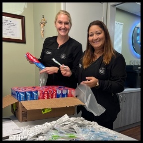 Two dental team members opening box filled with toothbrushes and tubes of toothpaste