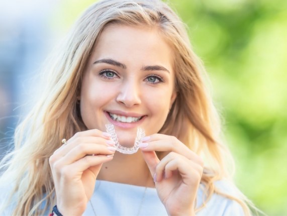 Smiling blonde woman holding an Invisalign aligner