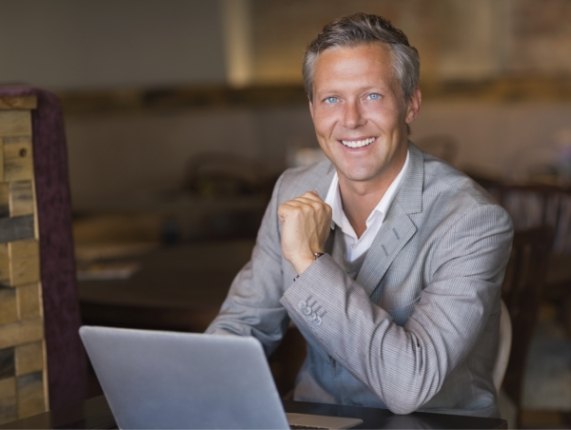 Smiling older man in gray suit sitting at table with laptop