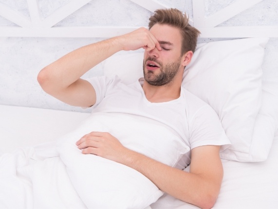 Man in bed with eyes closed pinching the bridge of his nose