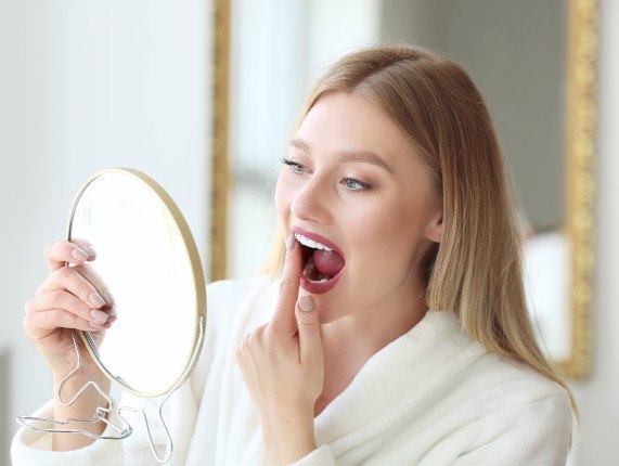 Woman looking at her teeth in handheld mirror