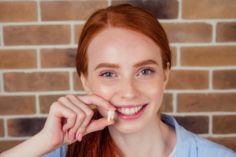 A smiling red-headed girl holding an extracted tooth