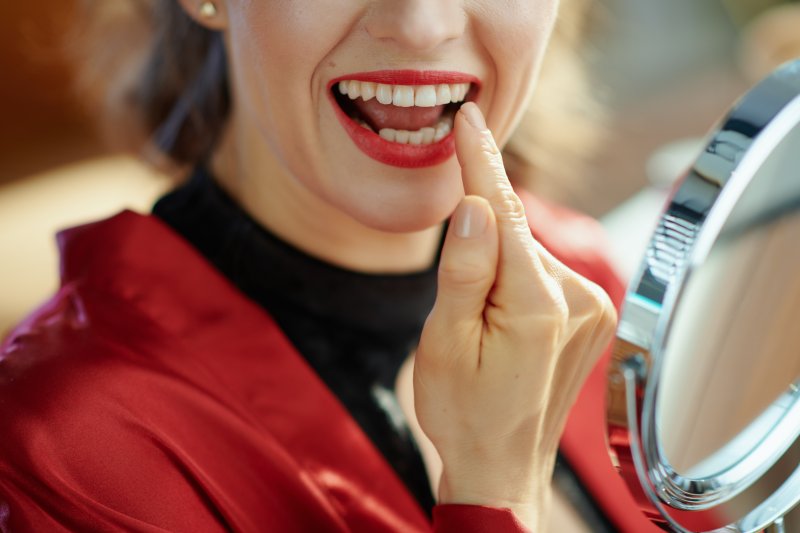 Woman looking at her dental bridge in a hand mirror