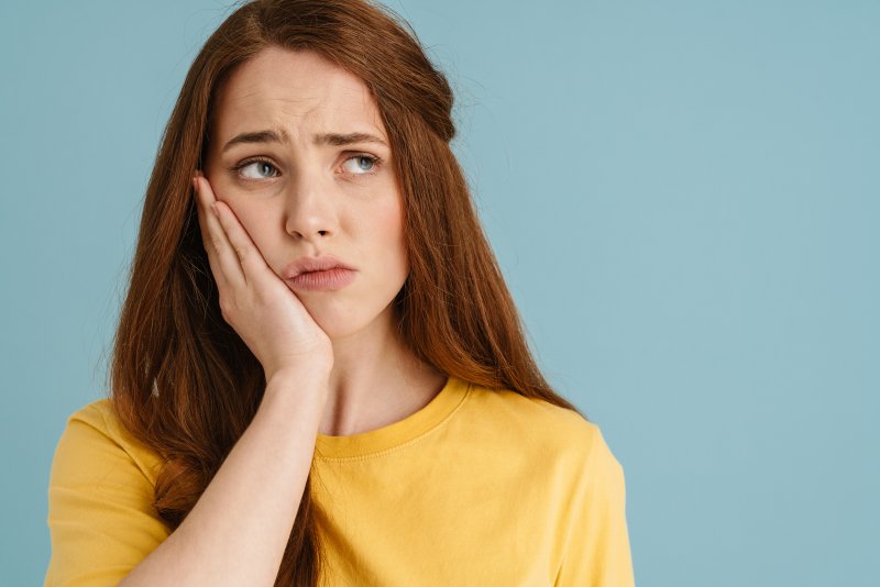 A woman holding her cheek because her dental bridge fell out