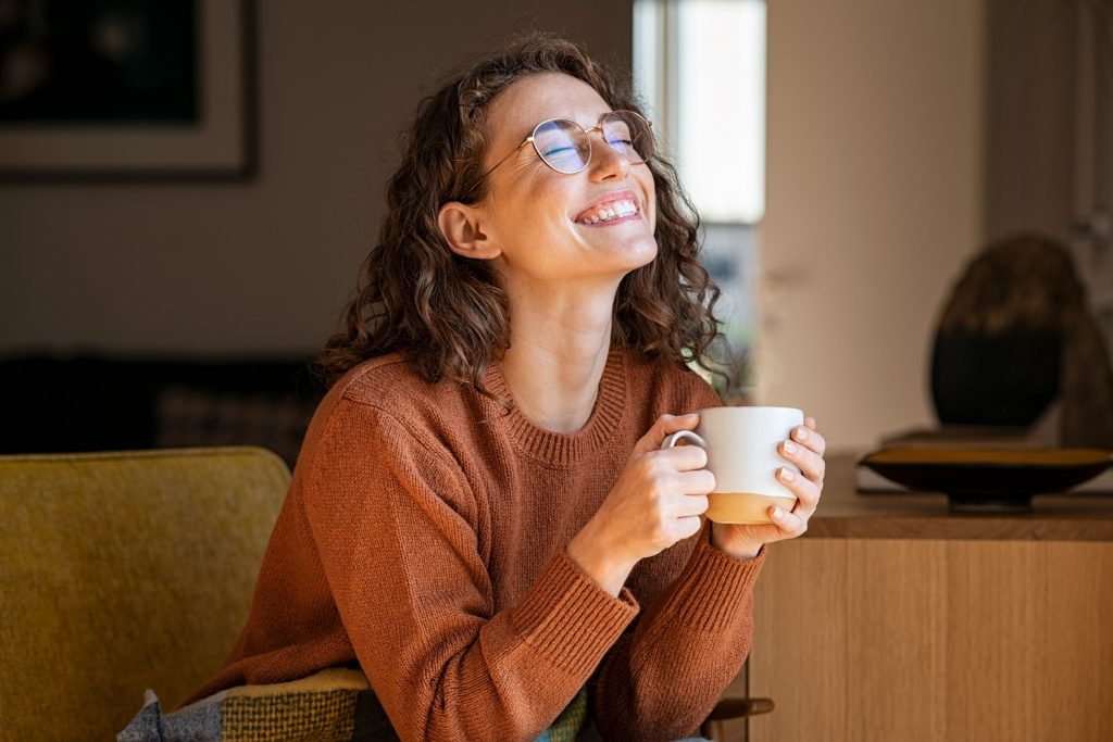Woman in brown sweater smiling while drinking coffee