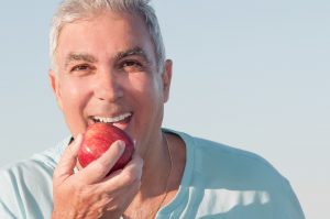 man biting into an apple with implant-retained denture