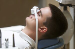 Man laid back in dentist’s chair wearing nasal gas mask.